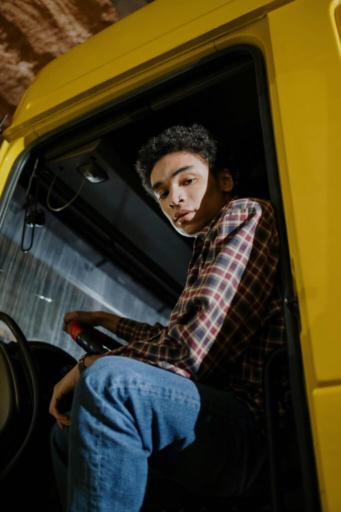A young man with curly hair seated inside a yellow truck, captured indoors at night.